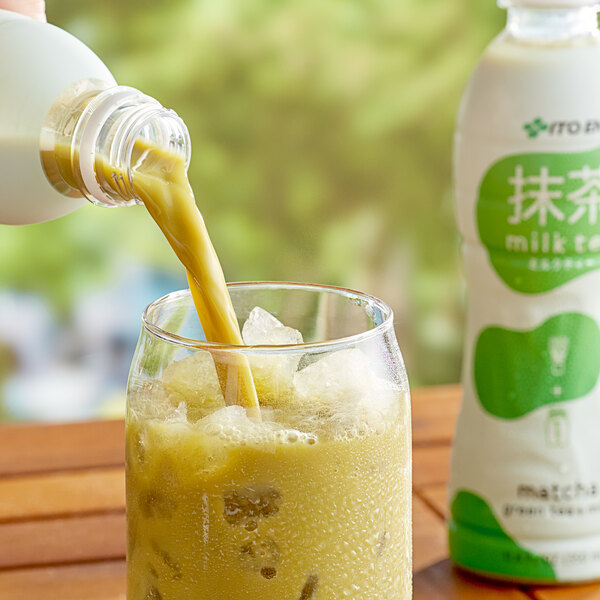 A hand pouring Ito En Matcha Green Iced Tea with Milk into a glass.