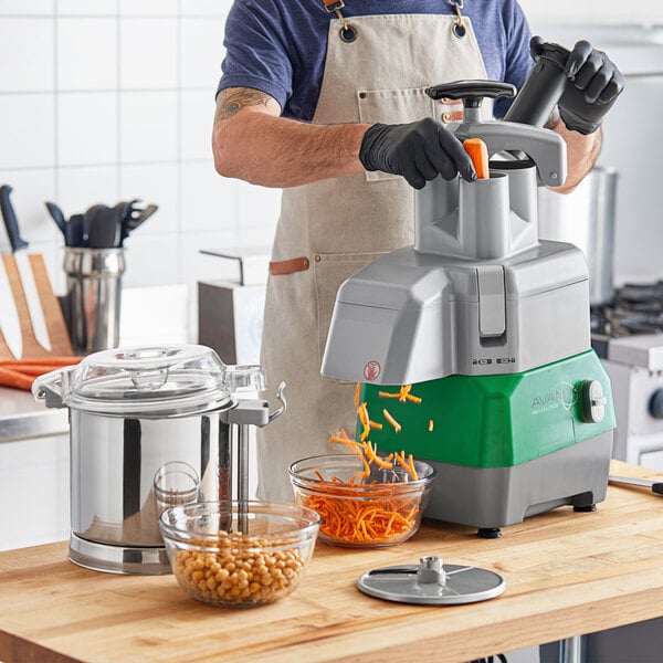 A man in an apron using the Avamix Revolution food processor to shred carrots into a bowl.