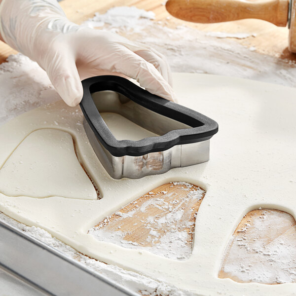 A person's hand wearing a white glove using a Wilton metal ghost cookie cutter to cut dough.