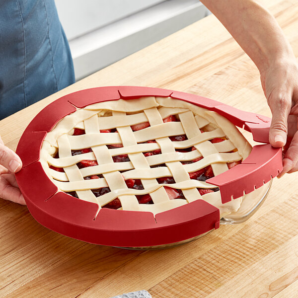 A hand using a red Wilton pie crust shield to cut a pie.