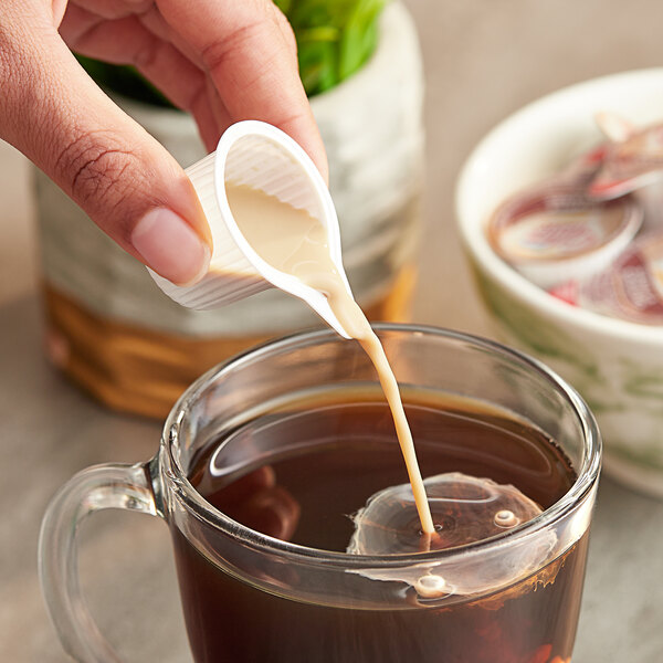 A hand pouring Nestle Coffee-Mate Vanilla Caramel creamer into a cup of coffee.
