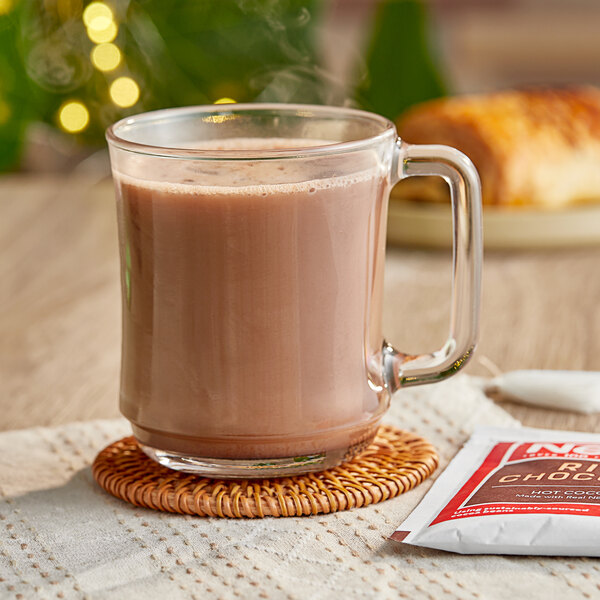 A glass mug of hot chocolate on a white coaster.