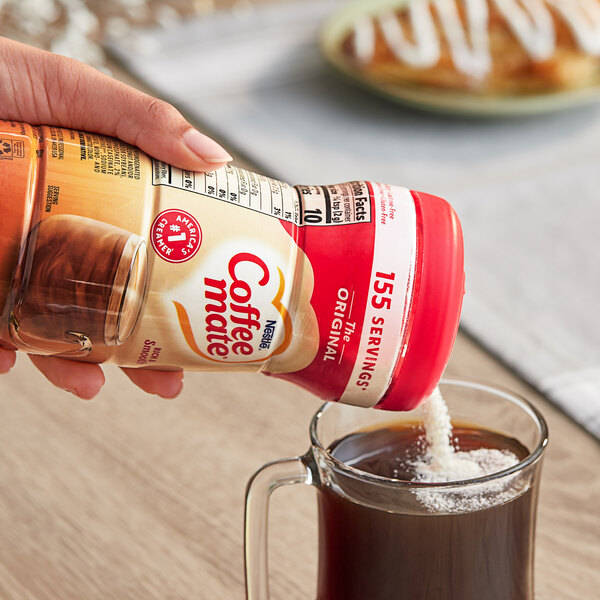A hand pouring Nestle Coffee-Mate into a glass of coffee.