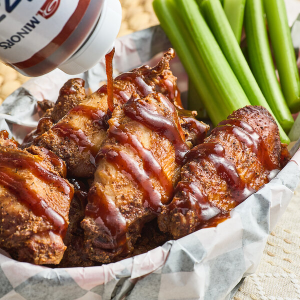 A person dipping chicken wings into a bowl of Minor's Drizzles Maple Bourbon BBQ Finishing Sauce.