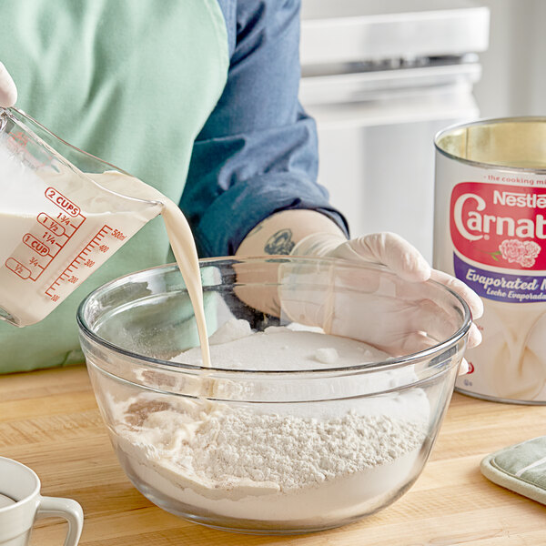 A woman pouring Carnation Evaporated Milk from a #10 can into a bowl.