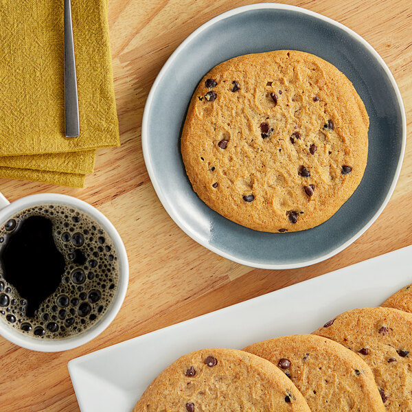 A plate with Otis Spunkmeyer chocolate chip cookies on it on a table with a cup of coffee.