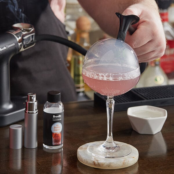 A person using a Breville commercial smoke bubble kit to pour a drink into a glass.