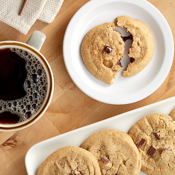 A close-up of an Otis Spunkmeyer milk chocolate chunk cookie on a plate next to a cup of coffee.