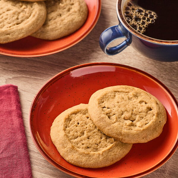 Two Otis Spunkmeyer peanut butter cookies on a red plate with a cup of coffee.
