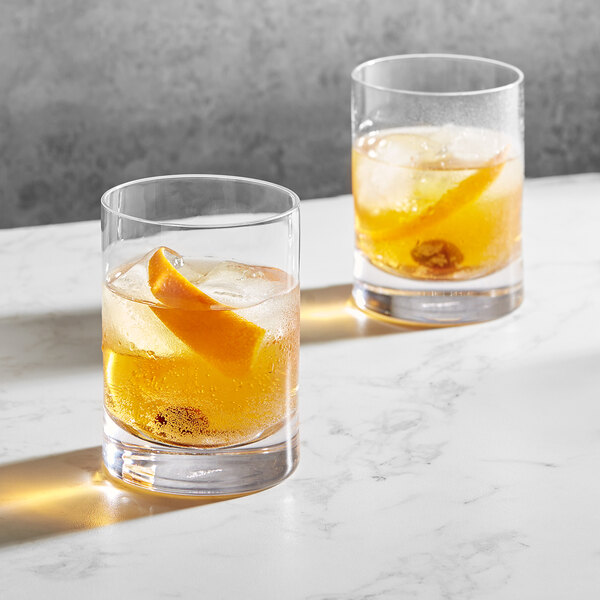 Two Della Luce Origins rocks glasses of whiskey with ice and orange slices.