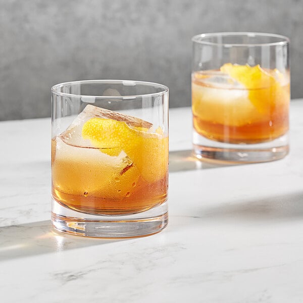 Two Della Luce rocks glasses filled with ice and whiskey with orange slices.