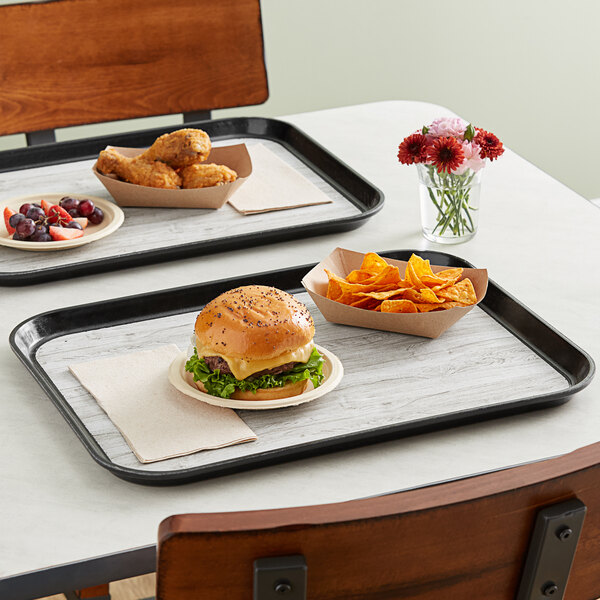 Two Dinex woodgrain and black non-skid trays with food on a table in a hospital cafeteria.