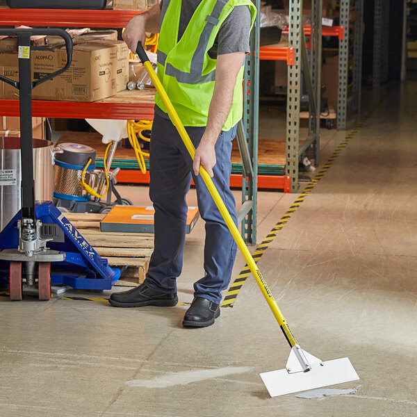 A man wearing a safety vest and using a Midwest Rake stainless steel scraper on a floor.