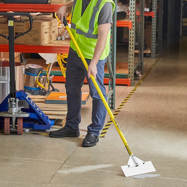 A person in a reflective vest using a Midwest Rake stainless steel scraper to clean a floor.