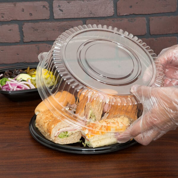 A person in a plastic glove putting a sandwich into a clear plastic container.
