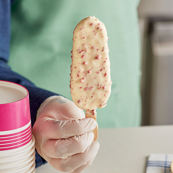 A person holding a Wicked Kitchen Vegan Berry White ice cream stick with sprinkles.