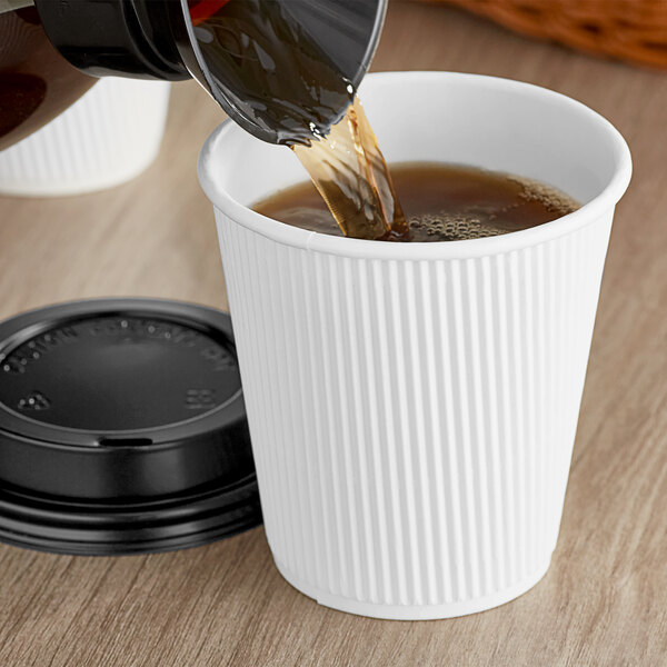 Choice white paper hot cup with black lid being filled with coffee.