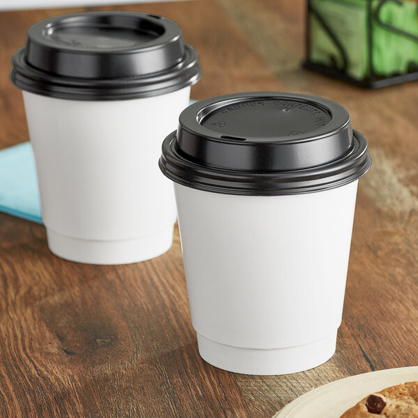 Two white Choice paper hot cups with black lids on a wooden surface.