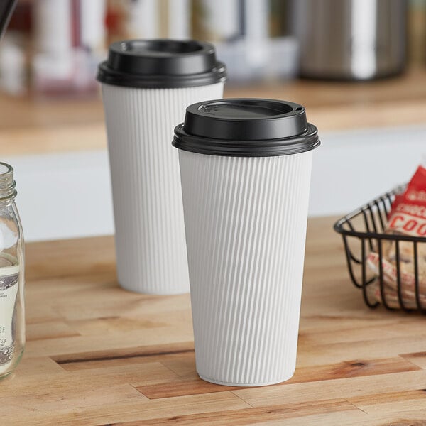 Two Choice white paper hot cups with black lids on a wooden surface.