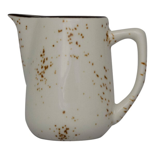 A white International Tableware creamer with brown speckles.
