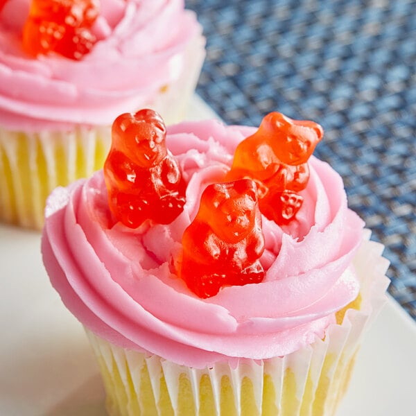A cupcake with pink frosting and a gummy bear on top.