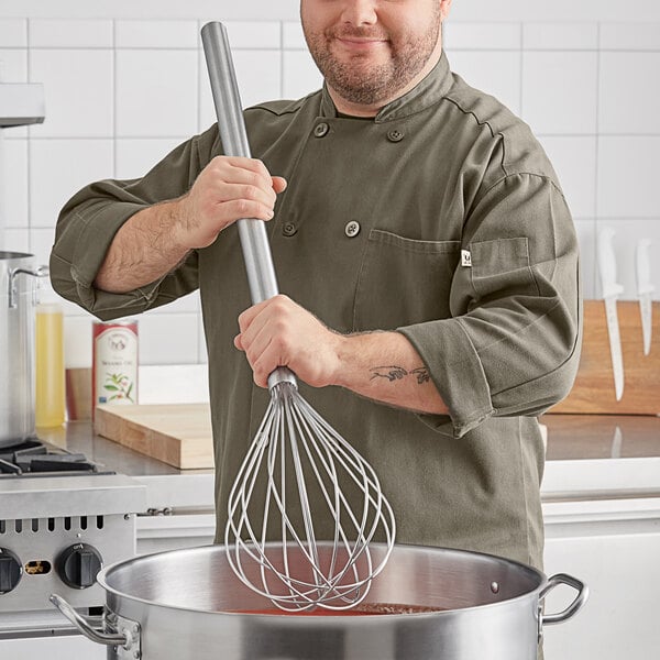 A man in a chef's uniform using a Choice stainless steel piano whisk in a pot.