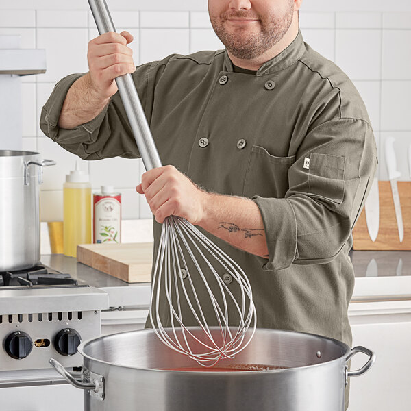 A man in a chef's coat using a Choice stainless steel piano whisk to stir a pot.