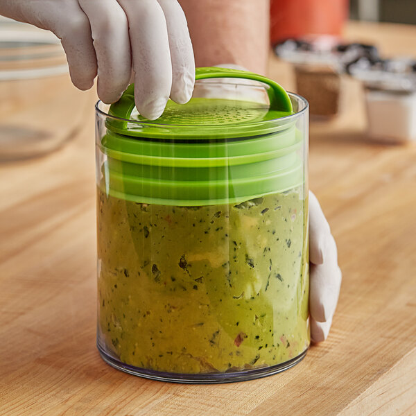 A person using a Prepara Evak Super Savor food storage container with a green lid to store food.