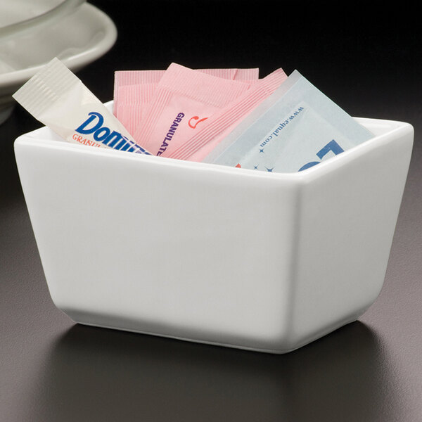 An American Metalcraft white porcelain sugar caddy on a hotel buffet counter filled with sugar packets.