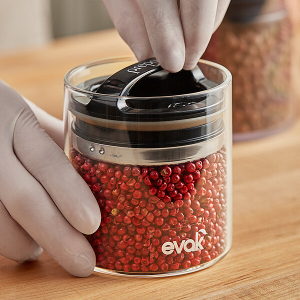 A person's hand using a Prepara Evak food storage container.
