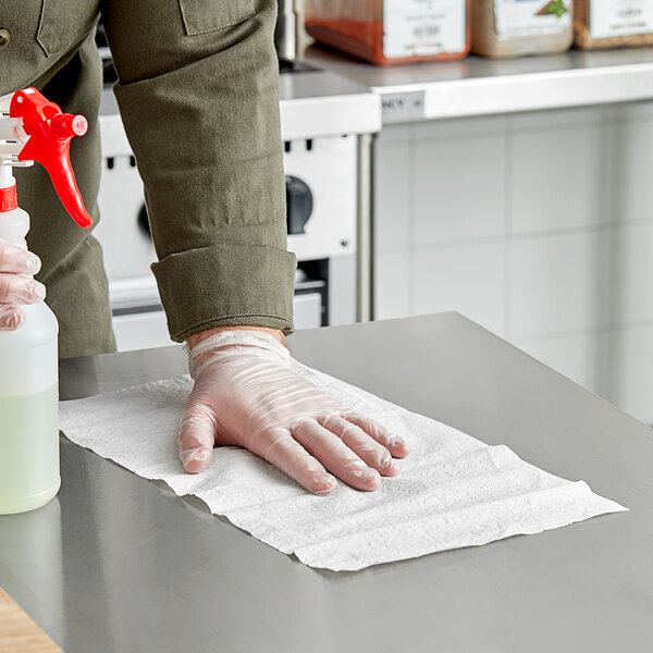 A person wearing gloves and using a Tork white paper wiper to clean a surface.