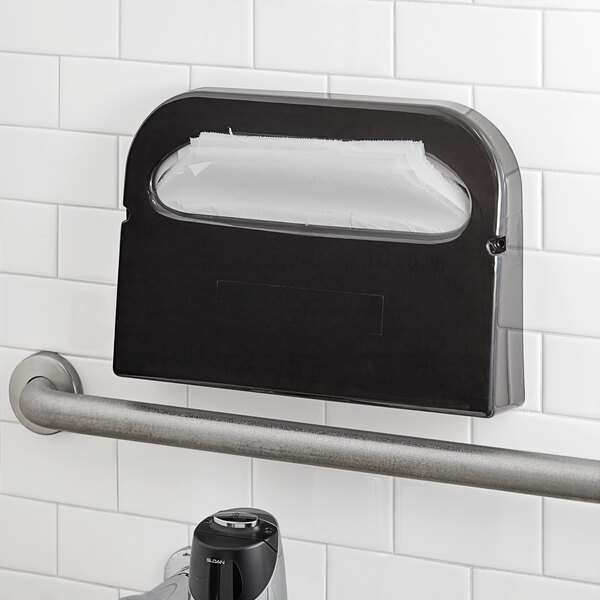 A black Tork toilet seat cover dispenser on a white wall.