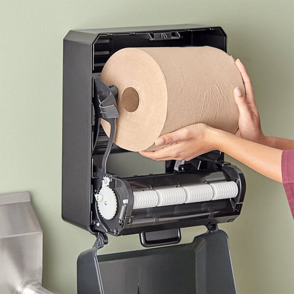 A person holding a roll of Tork Universal natural paper towels.