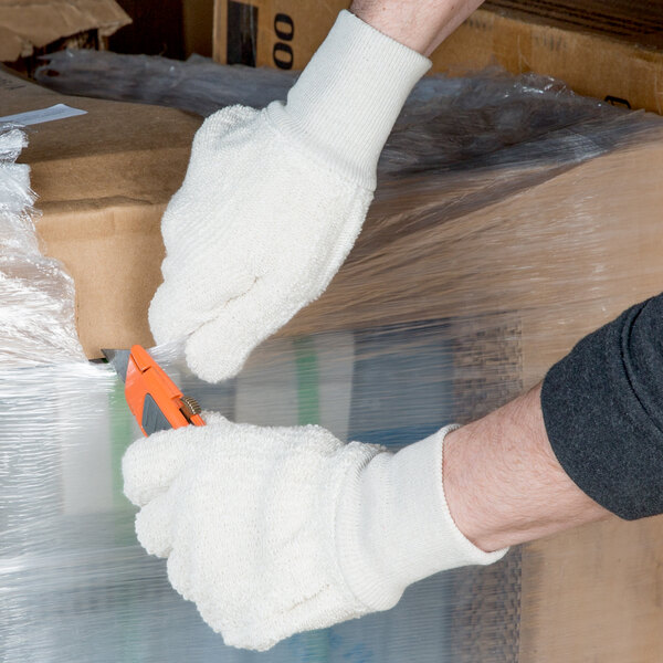 A person wearing Cordova loop-out terry work gloves cutting open a box with a knife.