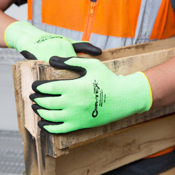 A person wearing Cordova Hi-Vis Lime gloves holding a piece of wood.