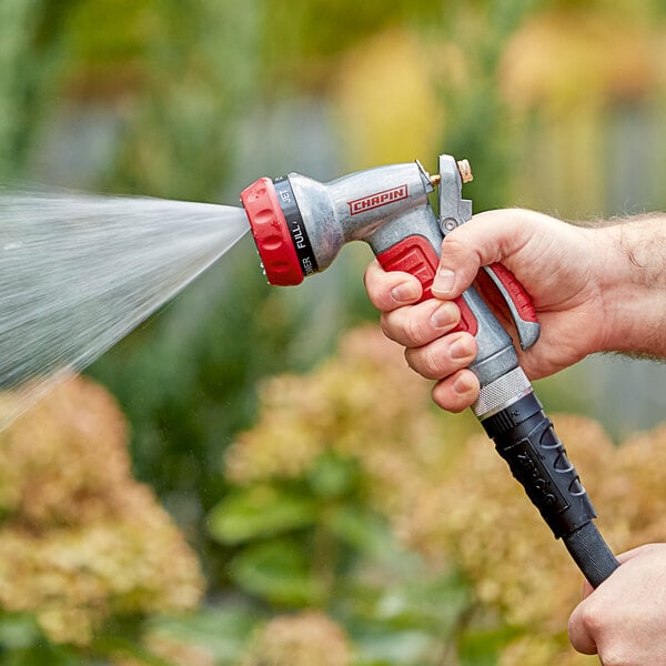 A person using a Chapin Die-Cast Metal 7-Way Premium Insulated Garden Spray Nozzle to spray water from a garden hose.