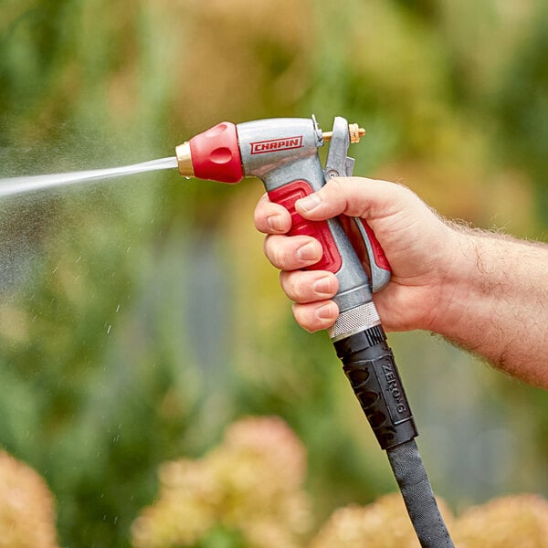 A hand holding a Chapin Die-Cast Metal Adjustable Insulated Garden Spray Nozzle spraying water from a hose.