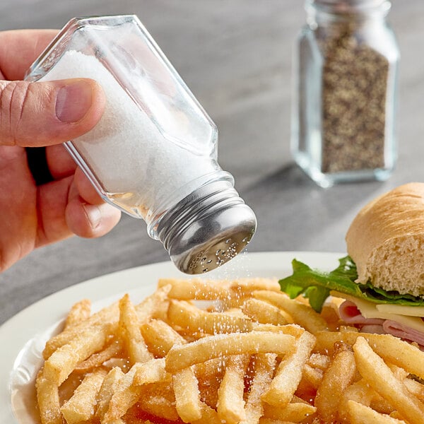 A hand holding a Choice square salt shaker over a plate of food.