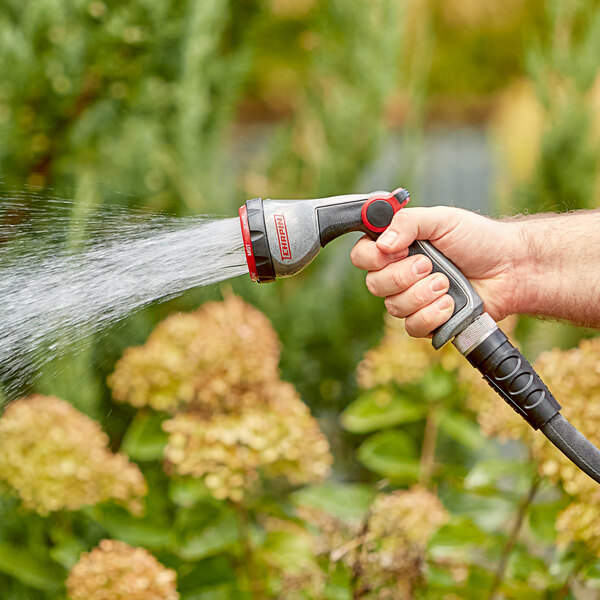 A hand holding a Chapin Die-Cast Metal 7-Way Deluxe Insulated Spray Nozzle spraying water from a garden hose.