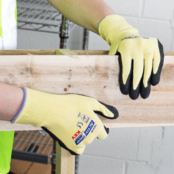 A person wearing Cordova ActivGrip Advance Kevlar gloves with black palm coating holding a piece of wood.