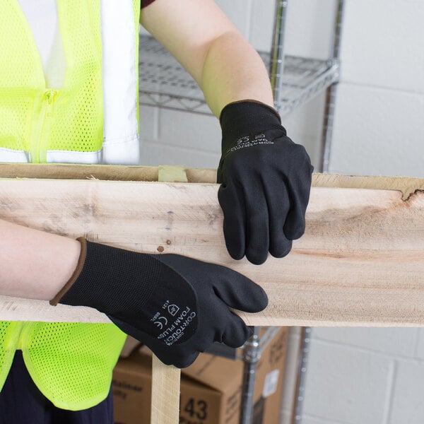 A person wearing Cordova black foam nitrile gloves holding a piece of wood.