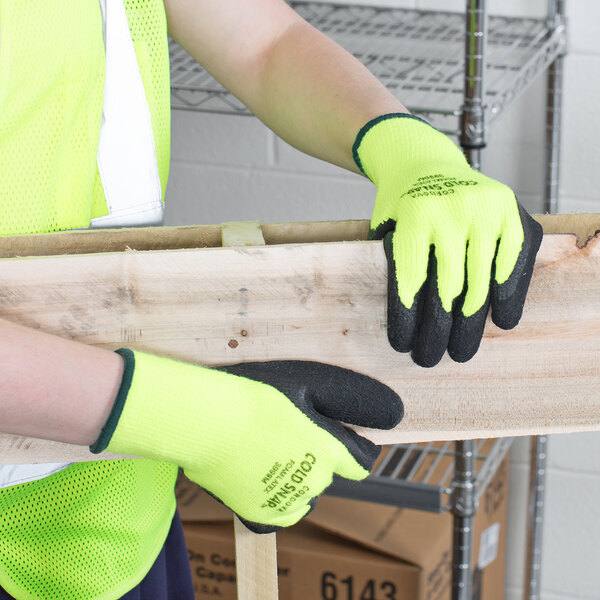 A person wearing Cordova Cold Snap safety gloves with black foam latex palm coating holding a piece of wood.