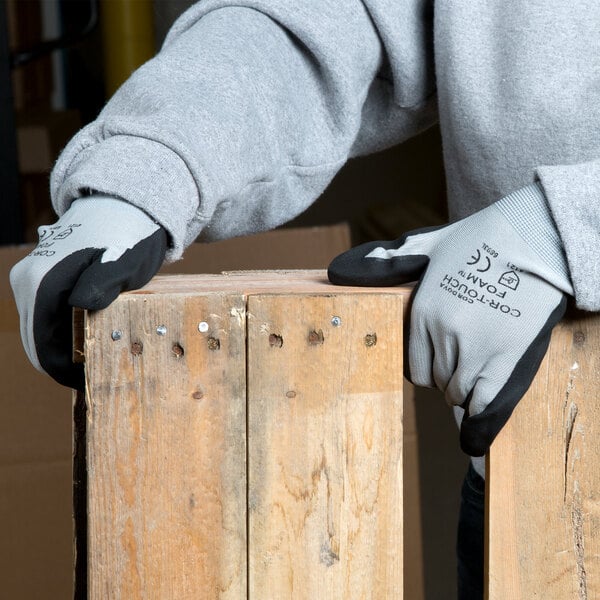 A pair of small gray Cordova Cor-Touch foam nylon gloves with black foam nitrile palms holding a piece of wood.