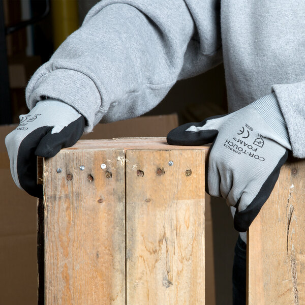 A person wearing gray Cordova Cor-Touch foam nitrile gloves holding a piece of wood.