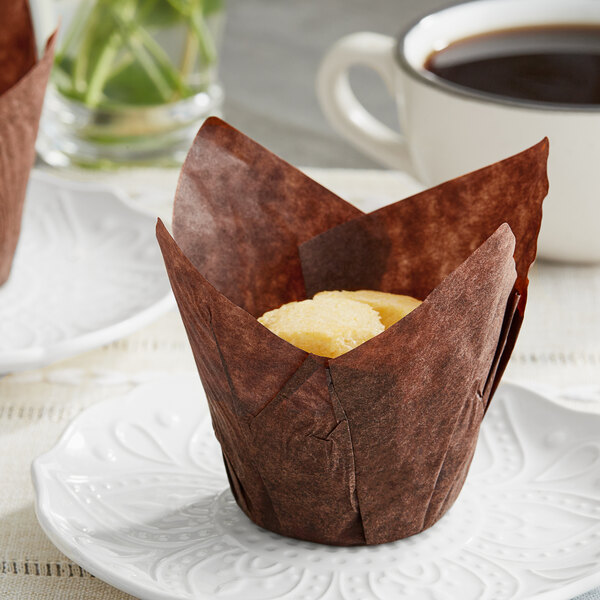 A Baker's Mark chocolate brown tulip baking cup with a cupcake inside on a plate.