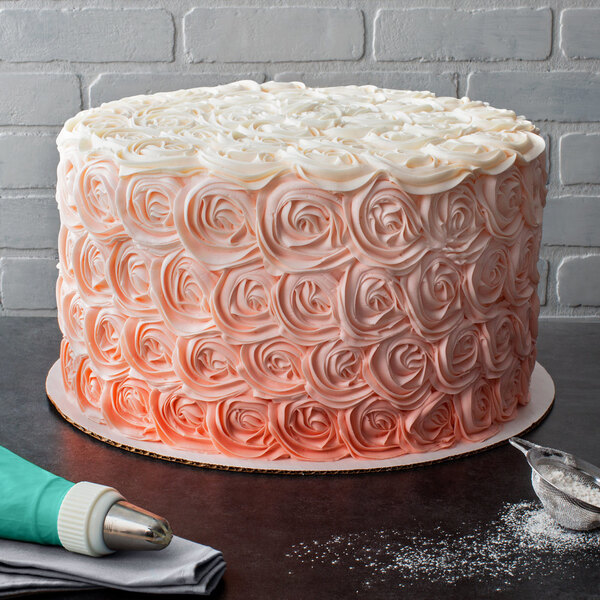 A Baker's Mark white cake circle with a cake with white and pink frosting on it.