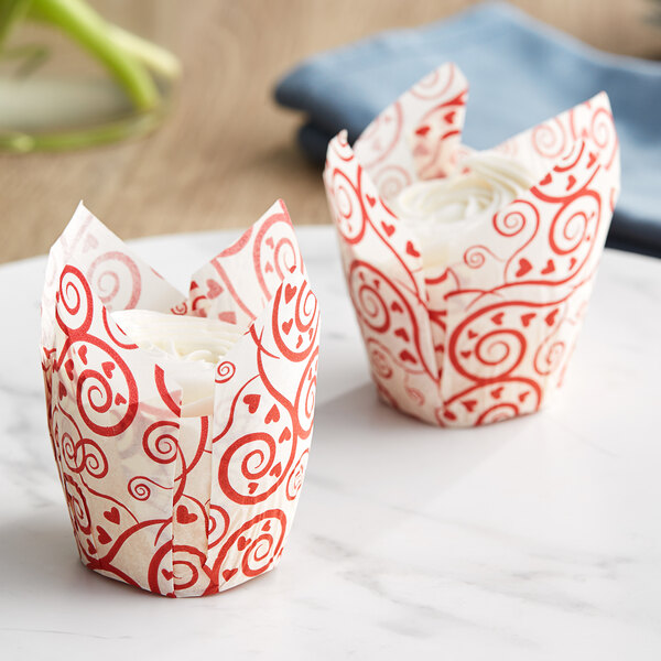 Two Baker's Mark tulip cupcake wrappers with a Valentine's Day design holding cupcakes on a marble table.