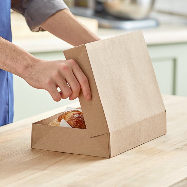 A person opening a Baker's Mark Kraft bakery box of doughnuts.
