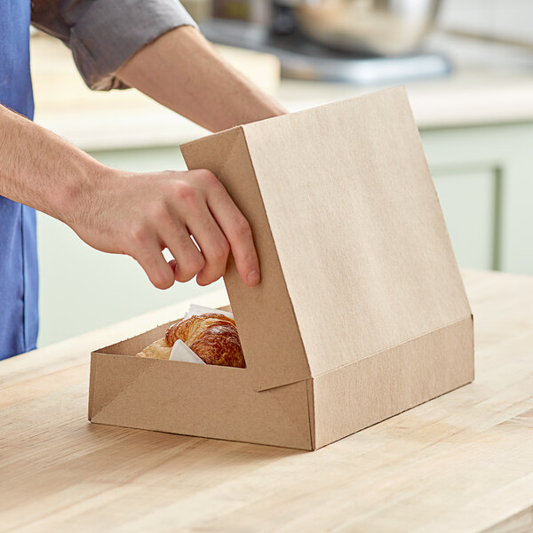 A person opening a Baker's Mark Kraft bakery box of doughnuts on a counter.