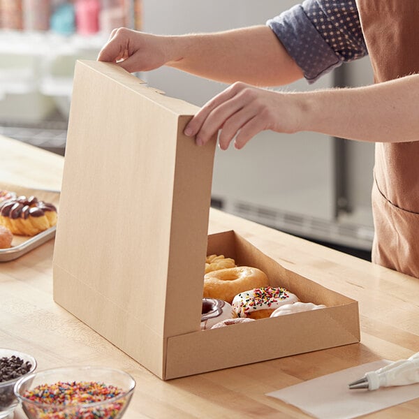A woman opening a Baker's Mark Kraft bakery box to reveal donuts.